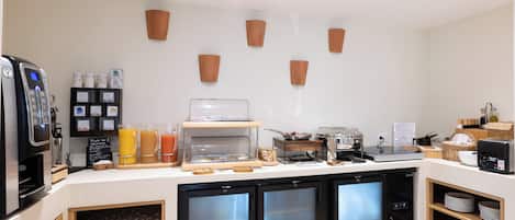 A modern breakfast bar with a coffee machine, juice dispenser, and refrigerated display case.