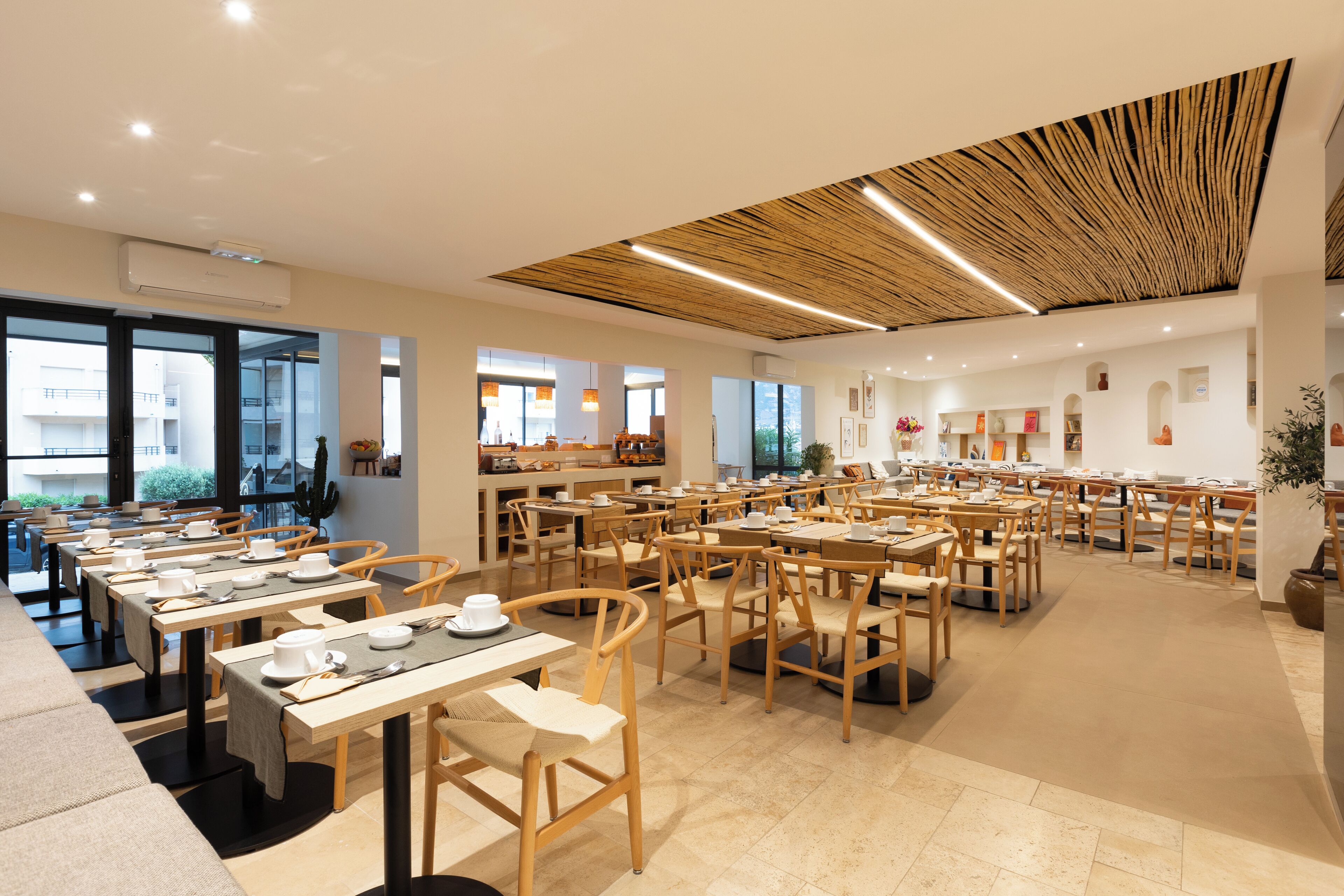 Una àmplia zona de dinar amb diverses taules i cadirees, grans finestres i un disseny de sostre modern.