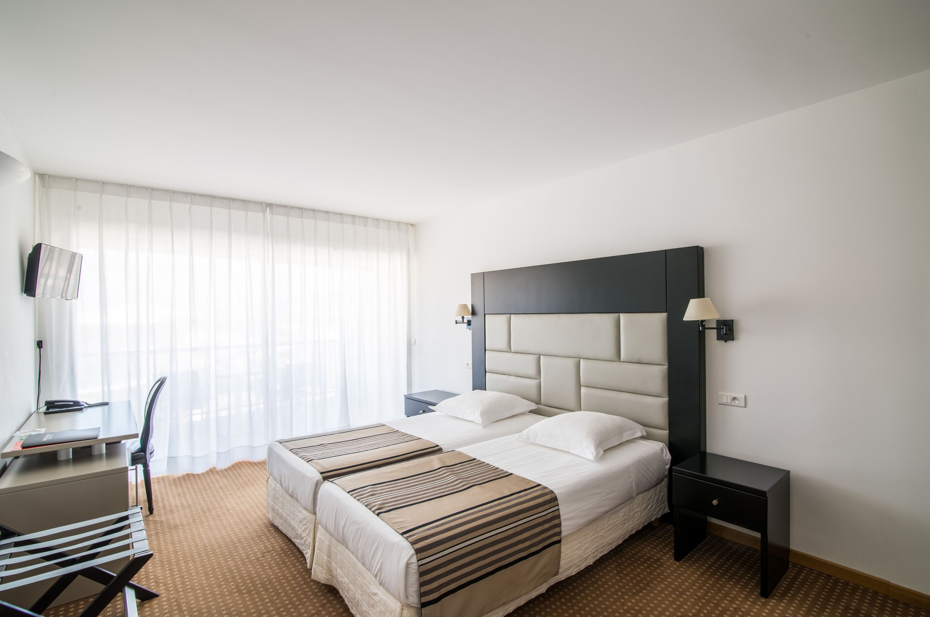A hotel room with a bed, bedside tables, a desk, and a chair.