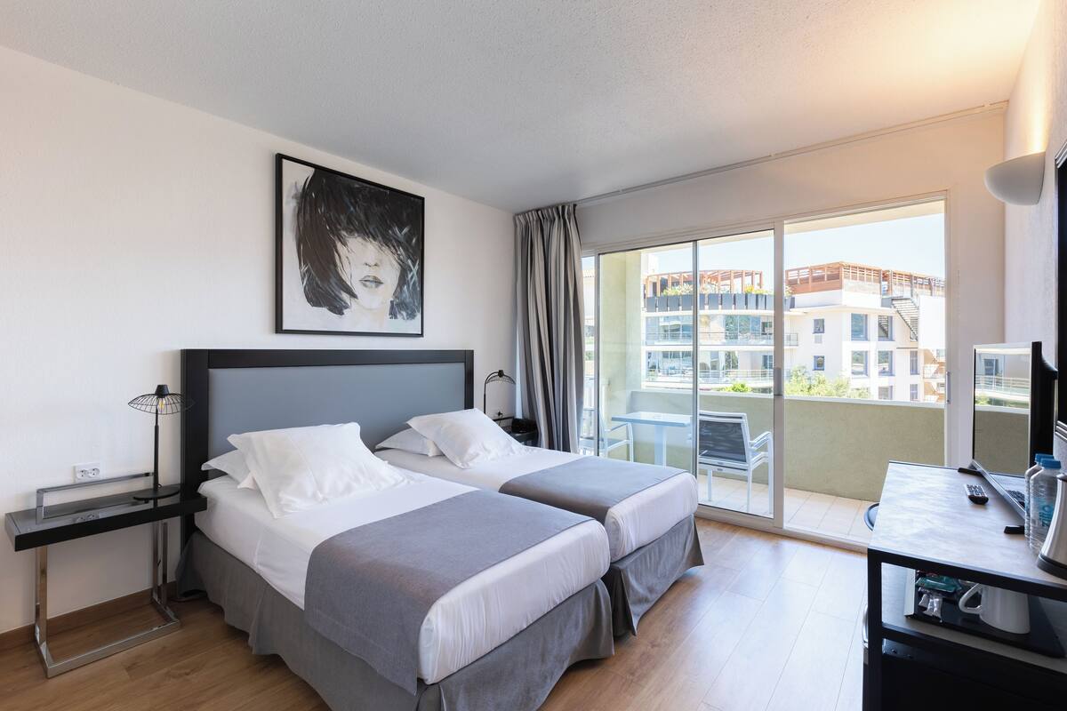 Una habitación de hotel moderna con dos camas, un escritorio, una silla y un balcón con vista a la ciudad.