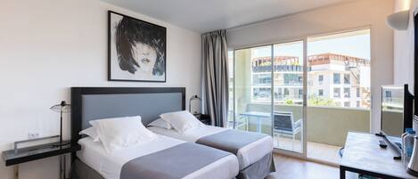 A modern hotel room with two beds, a desk, a chair, and a balcony with a city view.
