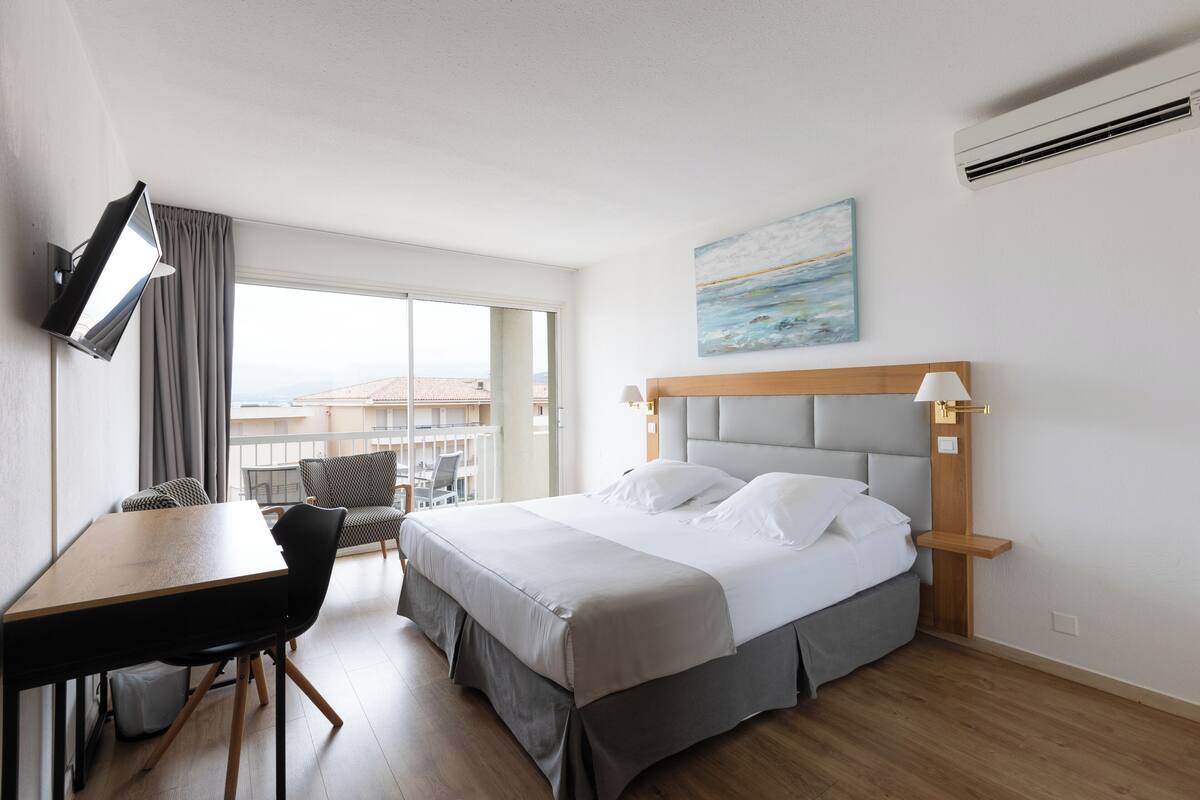 Una habitación de hotel con cama, escritorio, silla, televisor y un cuadro en la pared.