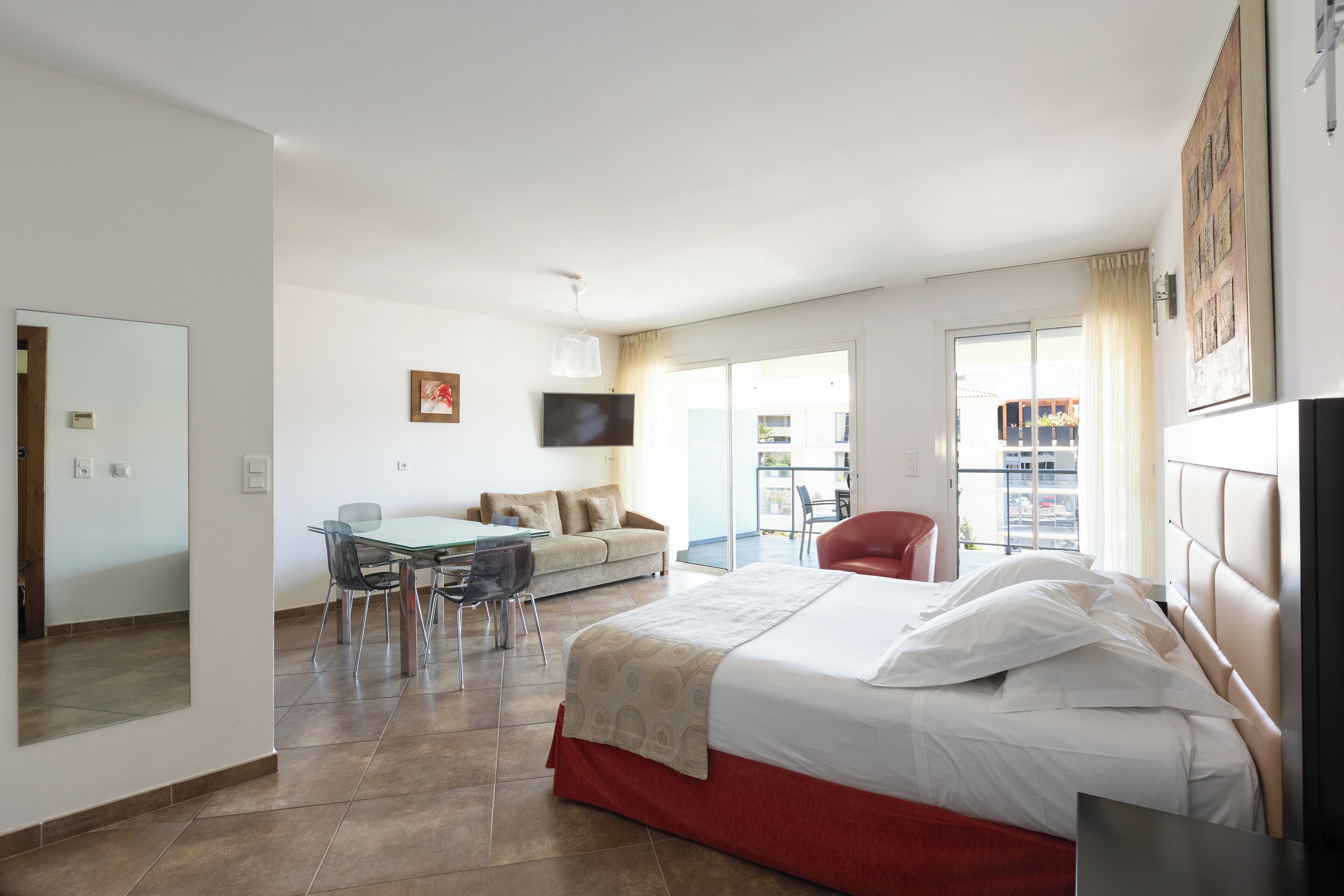 Ein Hotelzimmer mit Bett, Esstisch mit Stühlen, einer Couch, einem Fernseher und einem Balkon mit Blick.