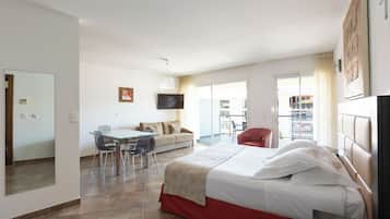 Ein Hotelzimmer mit Bett, Esstisch mit Stühlen, einer Couch, einem Fernseher und einem Balkon mit Blick.