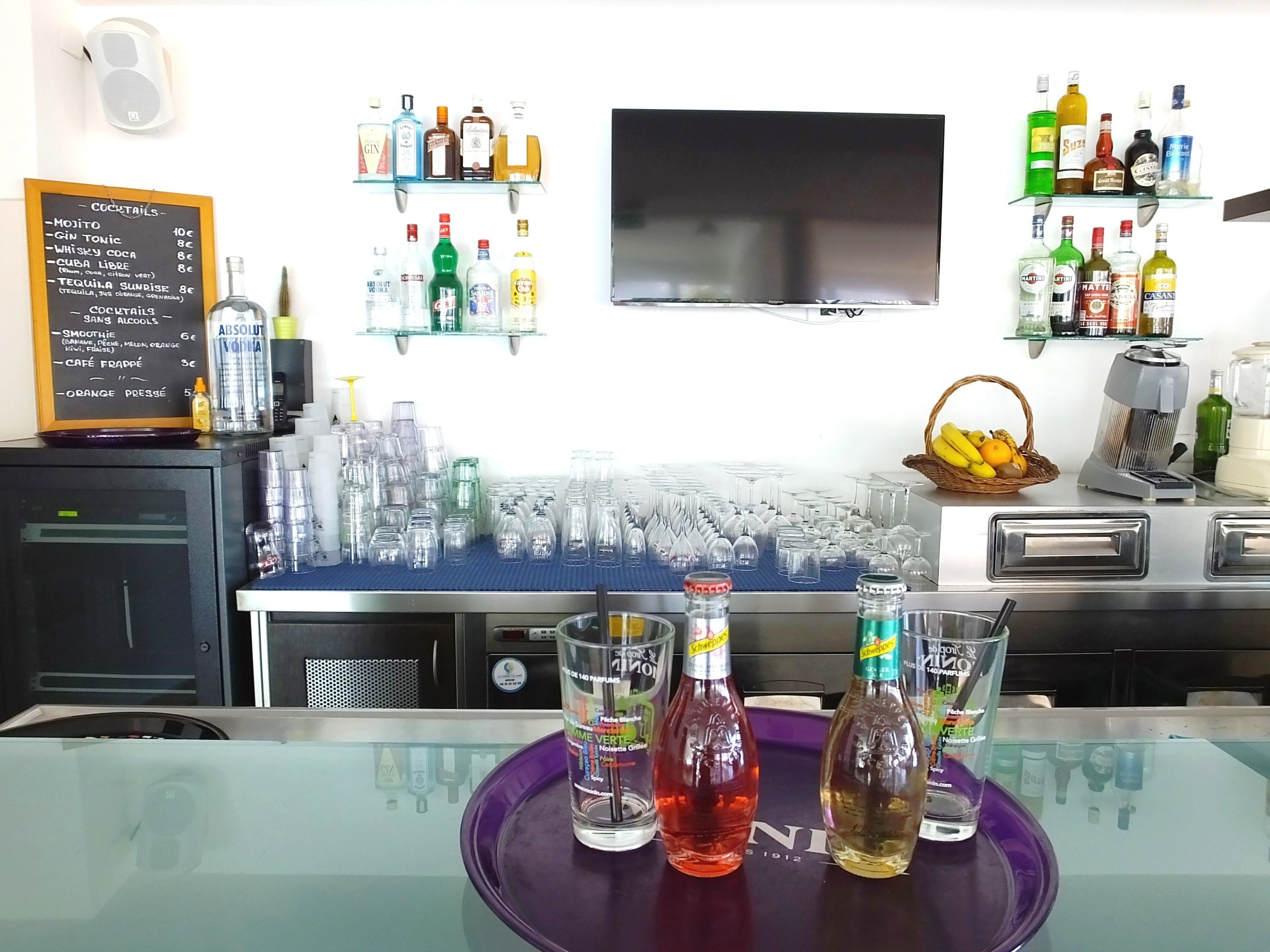 Zona de bar con una variedad de botellas de licores, vasos y un menú en pizarra que enumera cócteles y precios.
