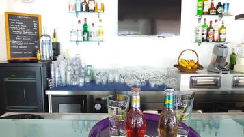 Zona de bar con una variedad de botellas de licores, vasos y un menú en pizarra que enumera cócteles y precios.