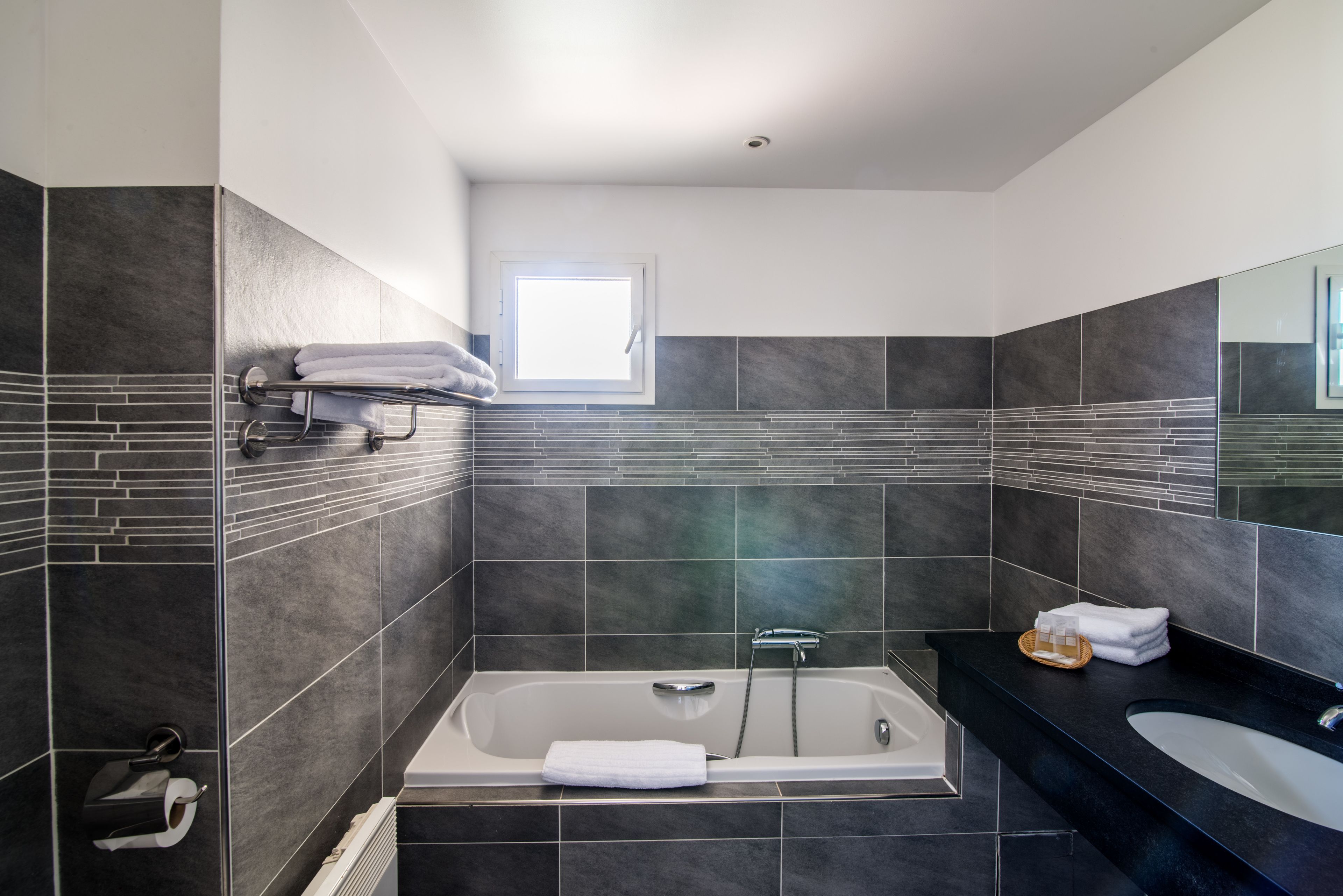Un baño moderno con bañera, tocador con espejo y ventana que proporciona luz natural.