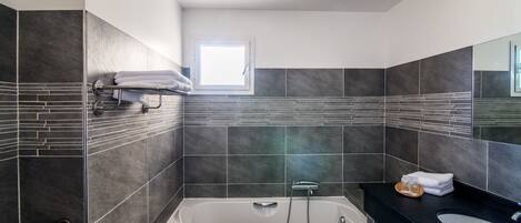 Un baño moderno con bañera, tocador con espejo y ventana que proporciona luz natural.