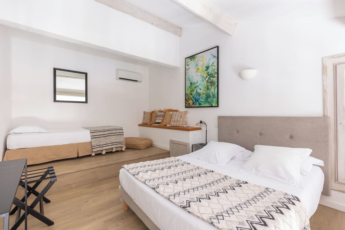 Un dormitorio moderno con una cama grande, una cama más pequeña, un escritorio y una silla. Hay un cuadro en la pared y una estantería con almohadones decorativos.