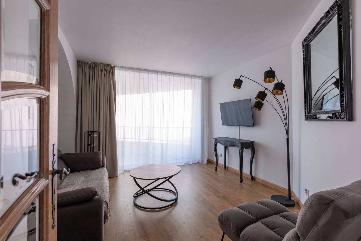 Una sala de estar moderna con un sofá, una mesa redonda de centro, un televisor y una lámpara de pie.