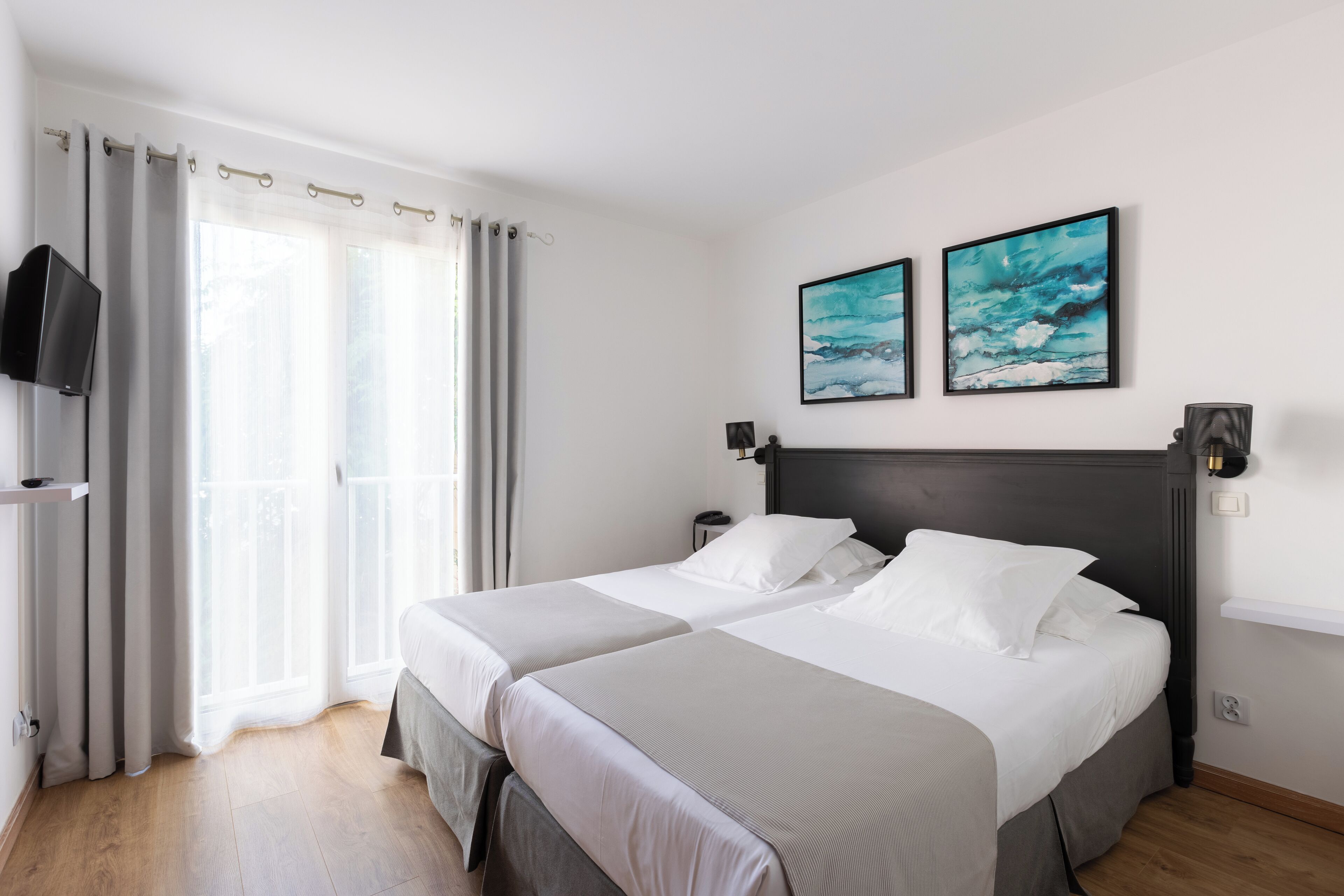 A hotel room with two beds, a TV, artwork, and a balcony.