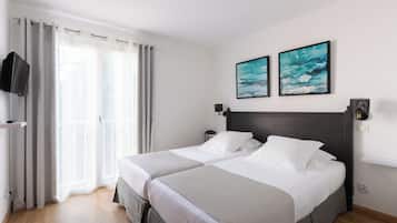 A hotel room with two beds, a TV, artwork, and a balcony.