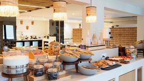 Ein reichhaltiges Buffet mit verschiedenen Speisen, darunter Gläser mit Aufstrichen, Schüsseln mit Frühstückscerealien und ein Schild mit der Aufschrift 'Frischer Blauer Käse'.