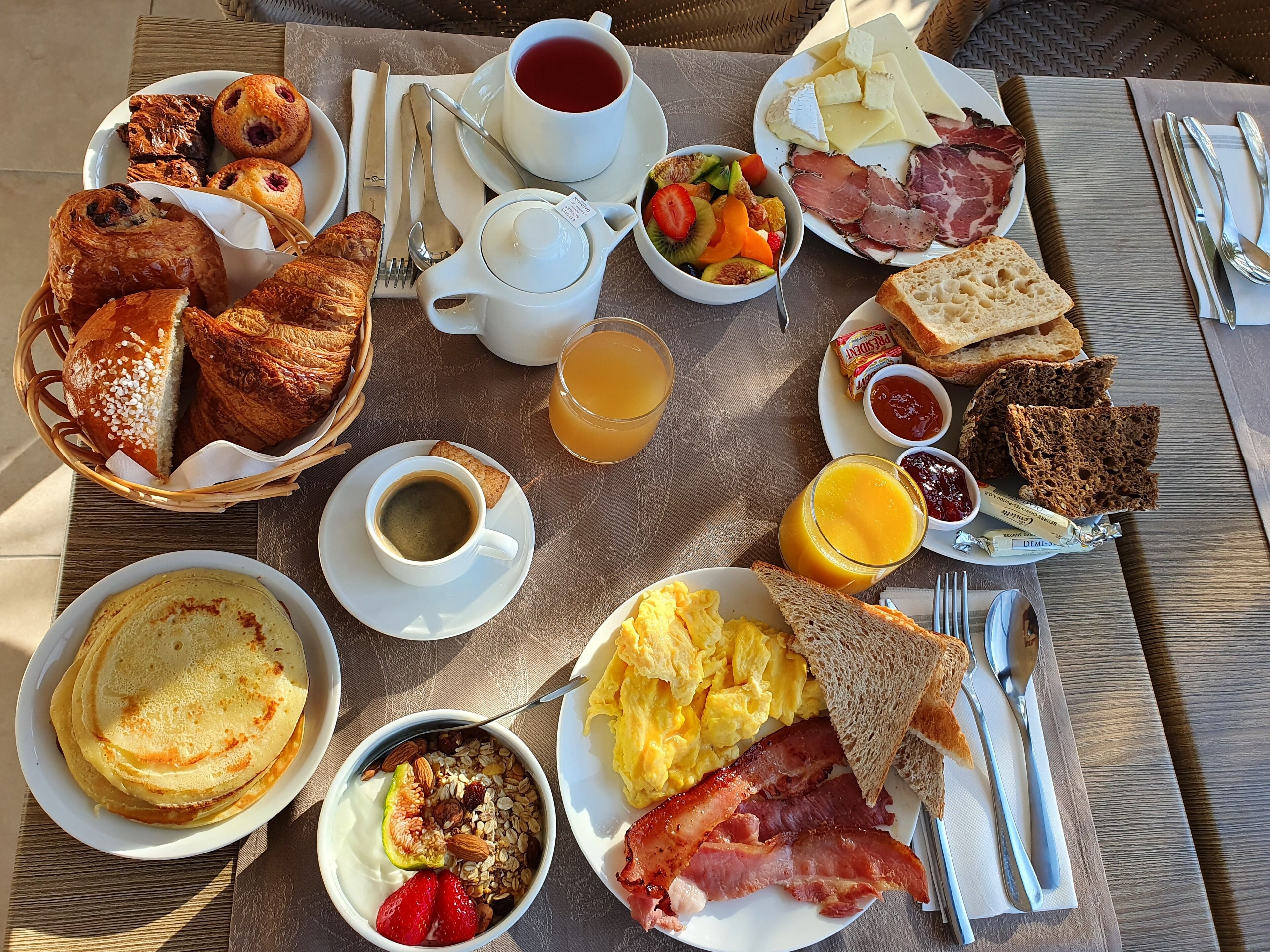 Un buffet de petit-déjeuner proposant une variété de plats, notamment des viennoiseries, des fruits, des œufs et de la charcuterie.