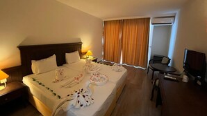 A hotel room with a large bed, a desk, a chair, and an air conditioning unit. - Palm Dor Hotel (Manavgat)