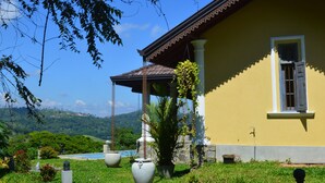 Um edifício amarelo com telhado de azulejos, uma janela com persianas e uma planta pendente.