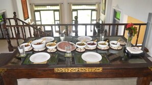 Mesa de jantar posta com várias tigelas de comida, copos e pratos, com uma escadaria e vista para o exterior ao fundo.