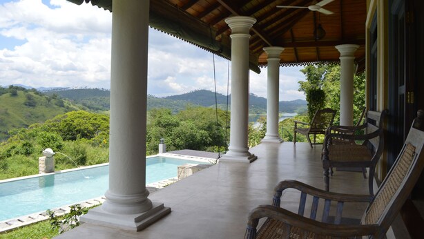 Área externa coberta com piscina, colunas brancas e cadeiras com vista para uma paisagem montanhosa.