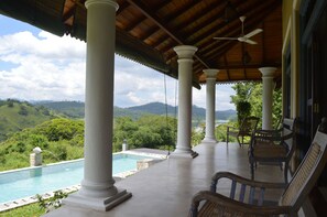 A covered outdoor area with a pool, white columns, and chairs overlooking a mountainous landscape. - Villa Tee Four (Maberiyatenna)
