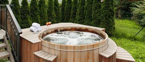 Una bañera de hidromasaje de madera con escalones, rodeada por una terraza de madera y un edificio de madera al fondo.
