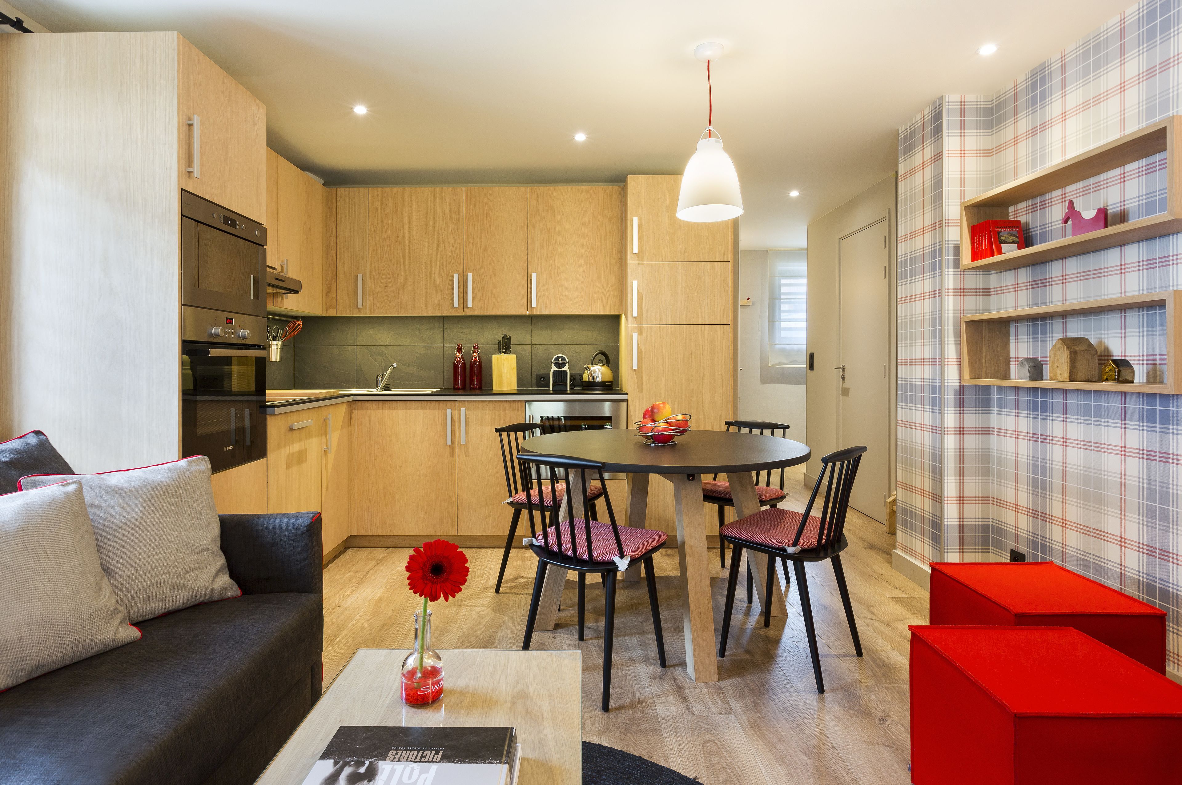 Une cuisine moderne avec des meubles en bois, une table à manger avec des chaises et un mur d’accent rouge.