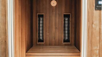 A sauna room with wooden walls, two windows with metal bars, a wooden ceiling, and a checkered floor.