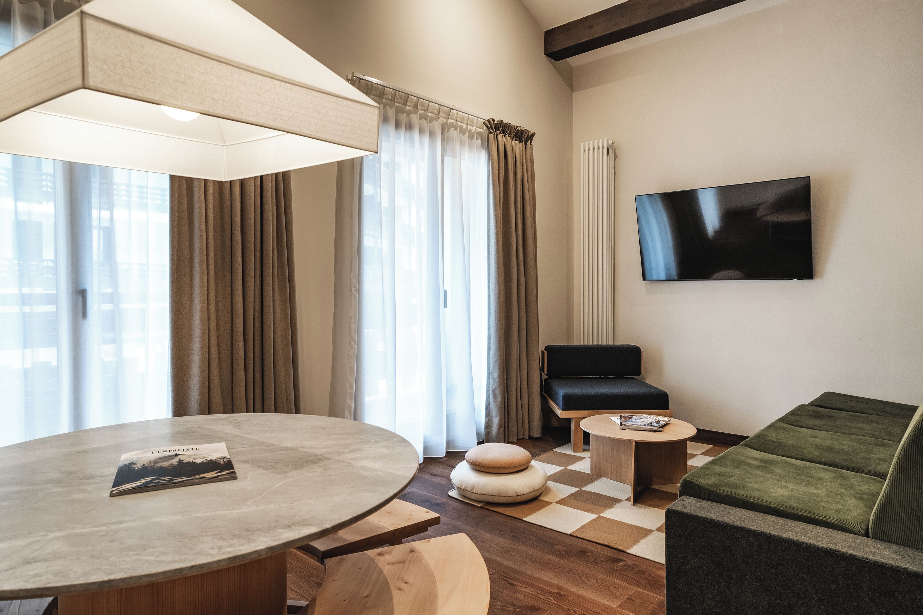 A modern living room with a round table, a sofa, a television, and a window with curtains.