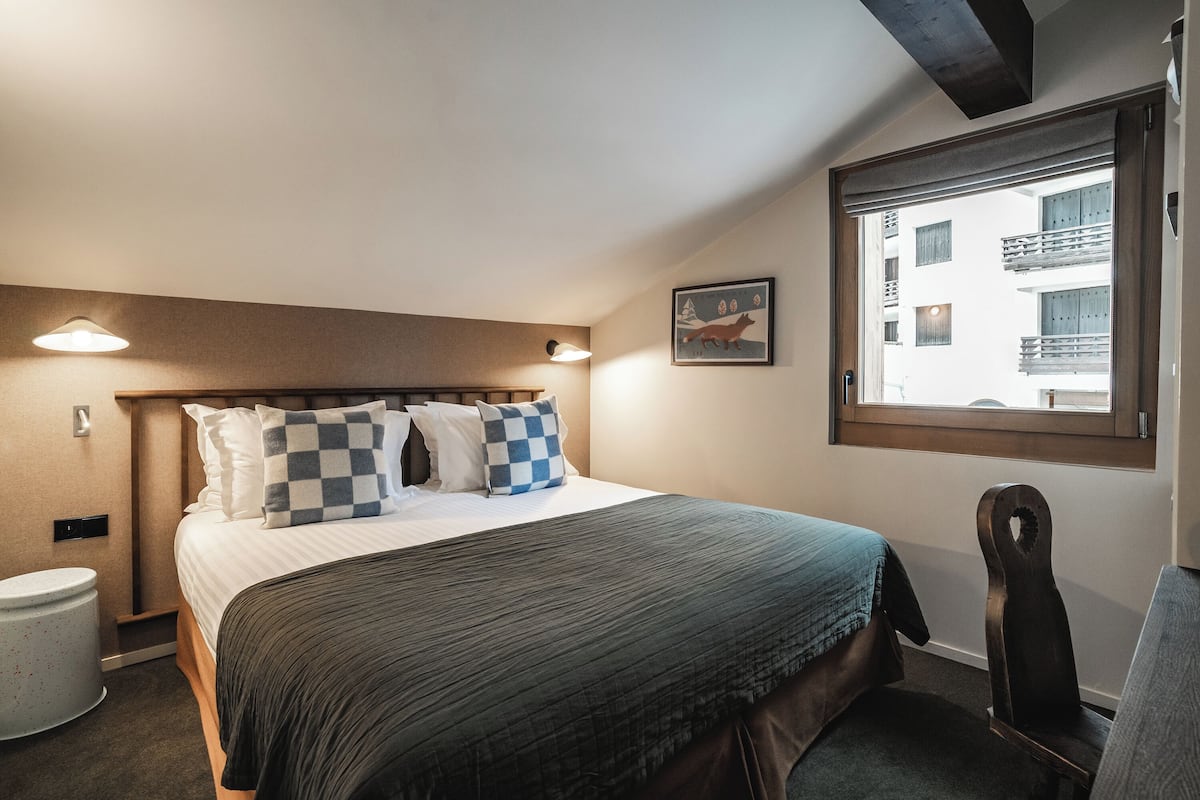 Et hotelværelse med en seng, en stol, et vindue og et billede på væggen.