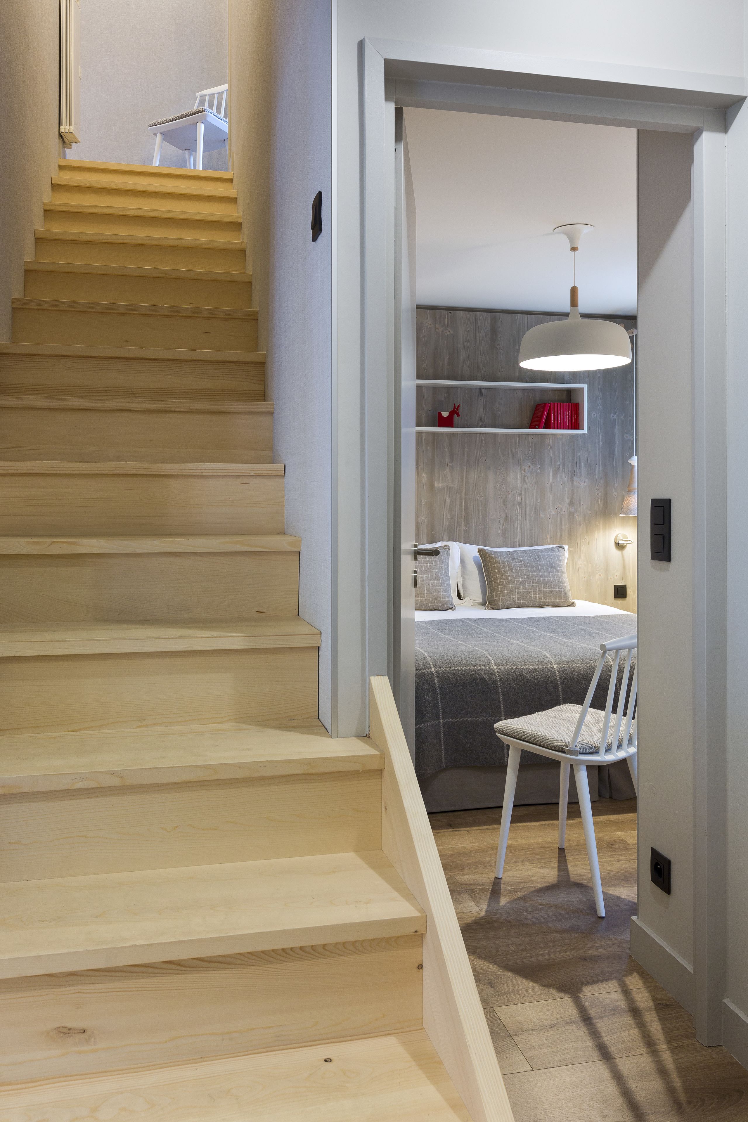 Escada que leva a um quarto com cama, uma cadeira e luminária pendente.