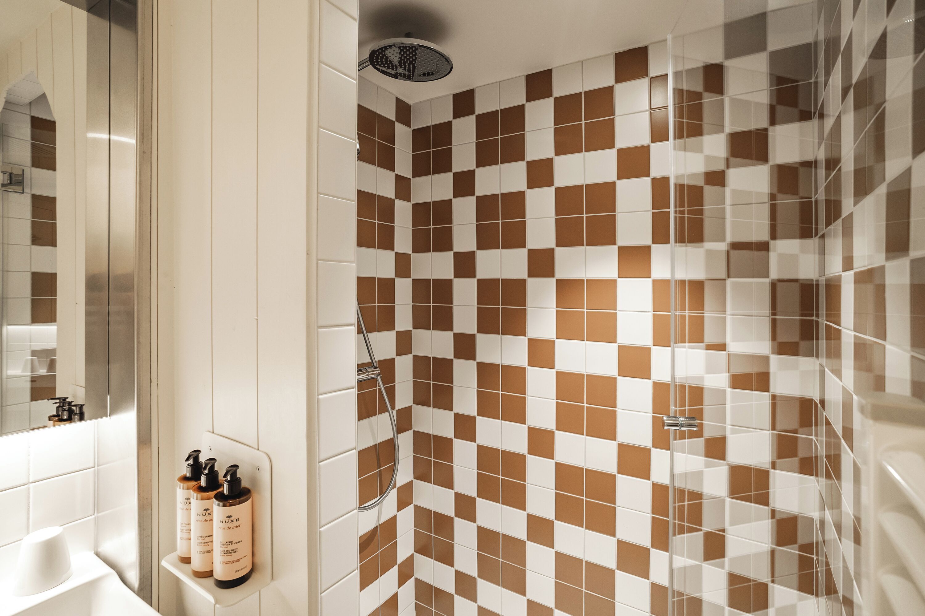 A bathroom with checkered tiles, a shower, and a shelf with toiletries.