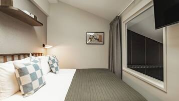 A neatly made bed with checkered pillows, a bedside lamp, a framed picture on the wall, and a window with curtains.