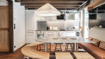 Una cucina moderna con isola centrale, mobili bianchi e un'area salotto con panche in legno.