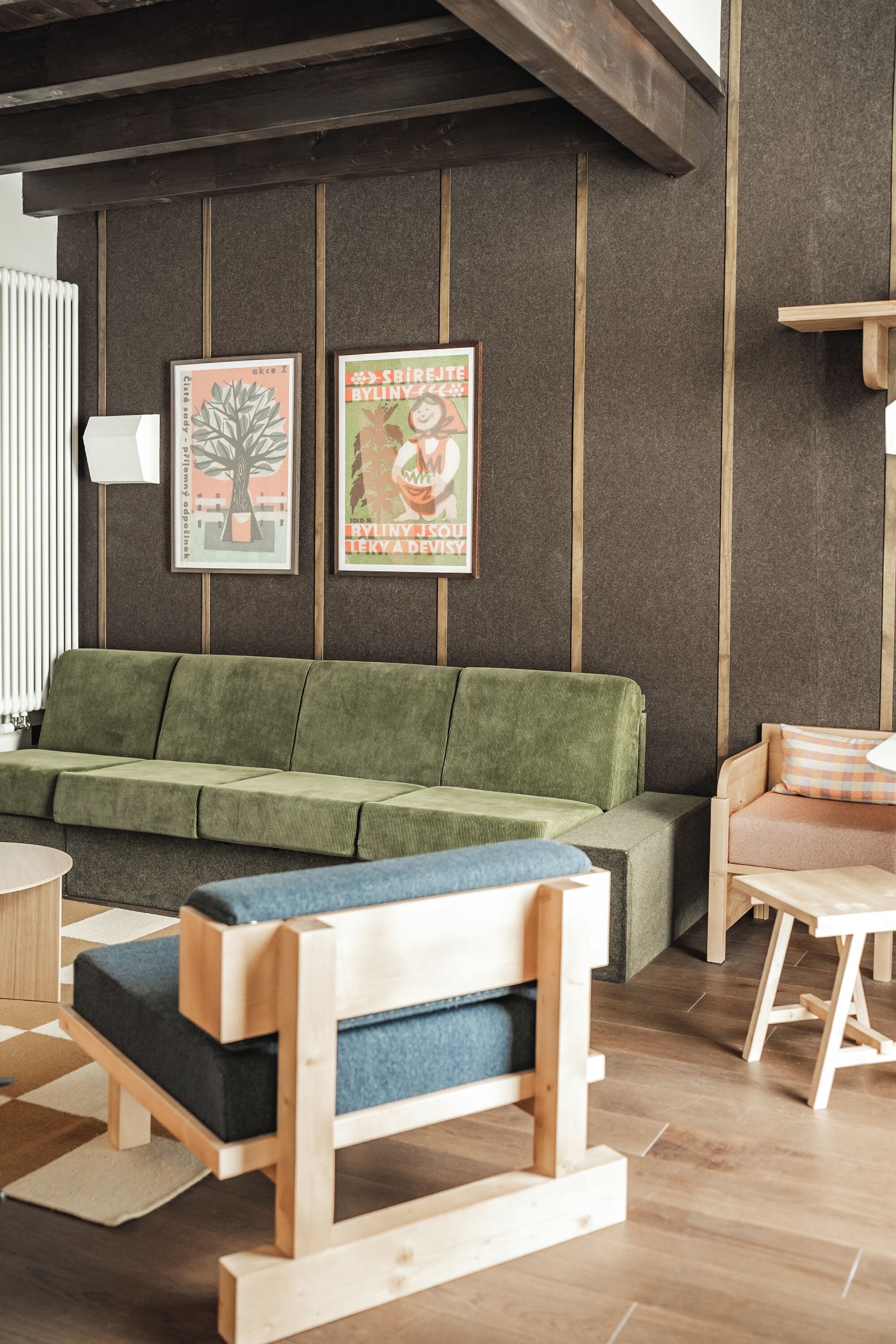 A modern living room with a green sofa, a wooden bench, and a small table. There are two framed posters on the wall.