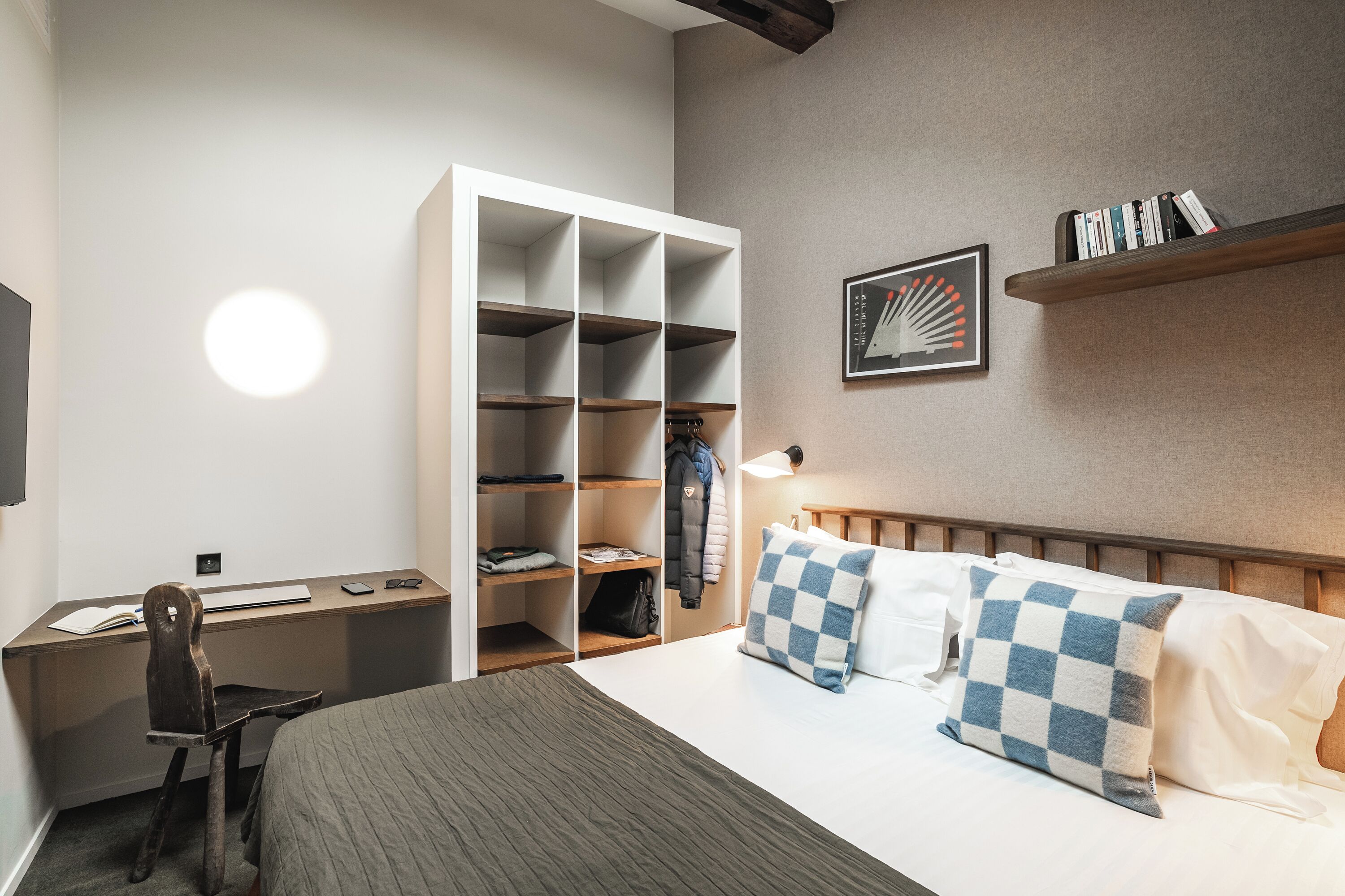 Una habitación de hotel ordenada con cama, escritorio, silla, armario y estantería con libros.