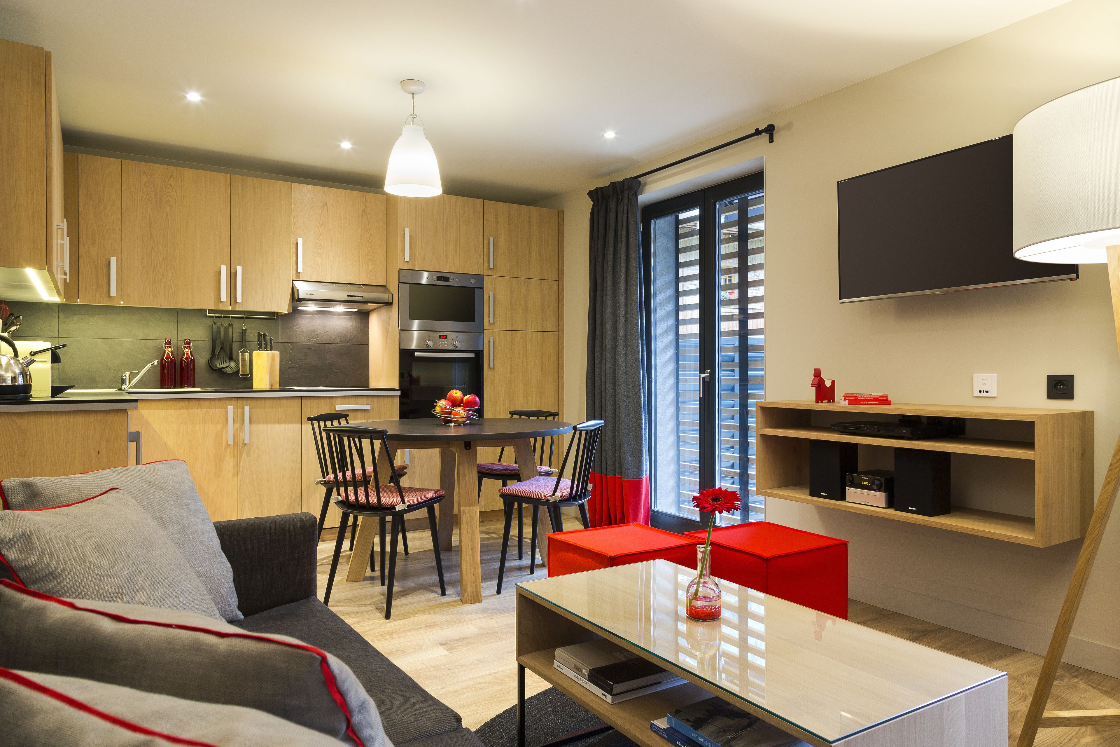 A modern kitchen with wooden cabinets, a dining area with a table and chairs, and a living room with a sofa and a coffee table.