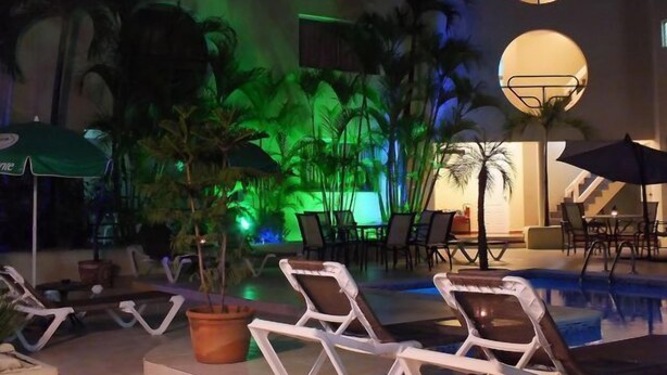 Zona de piscina con sillones de descanso, sombrillas y plantas en macetas.