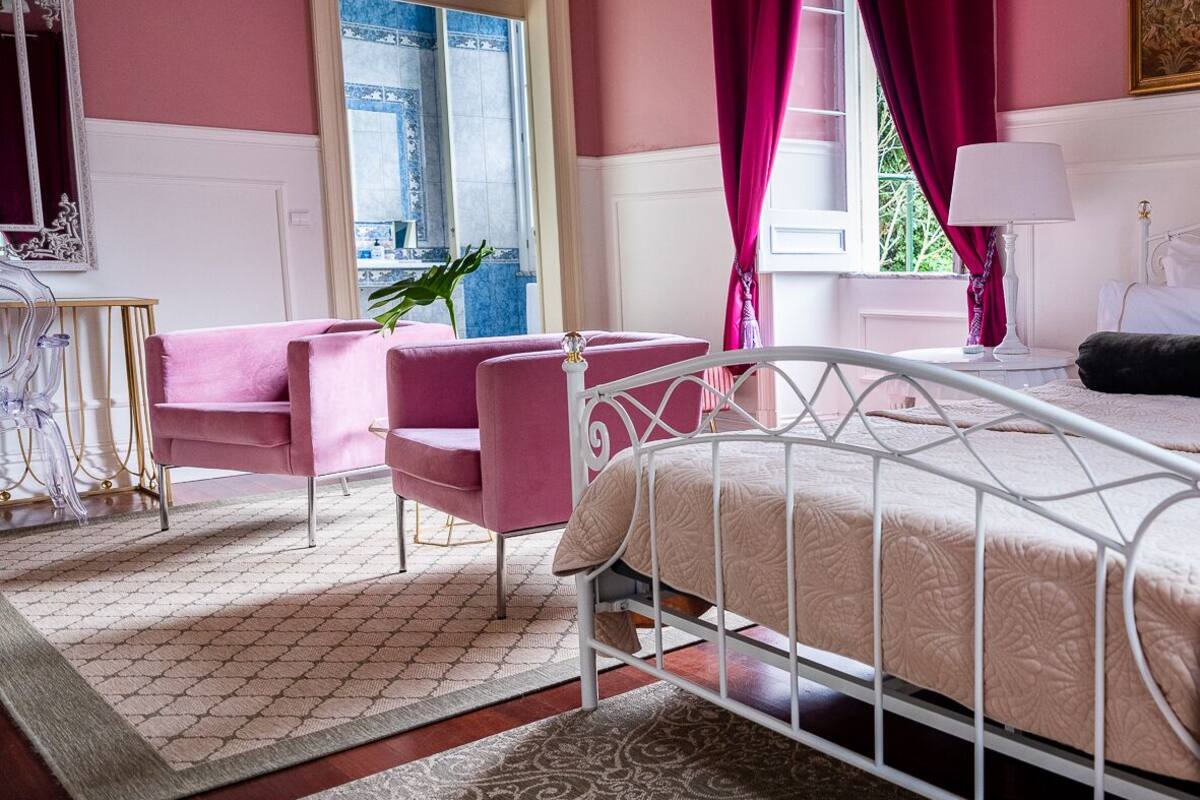 A bedroom with a bed, a chair, a table, and a window with curtains.