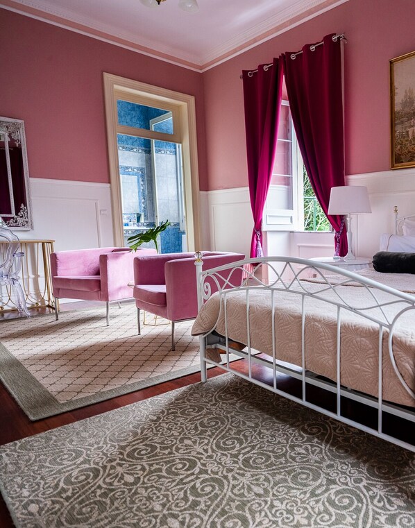 A bedroom with a bed, a chair, a table, and a window with curtains.