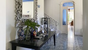 Un couloir avec une console noire, un miroir décoratif et un escalier menant à une autre pièce.
