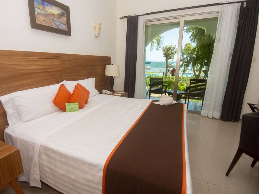 A hotel room with a bed, a nightstand, a lamp, a view of the ocean through a glass door, and a chair.