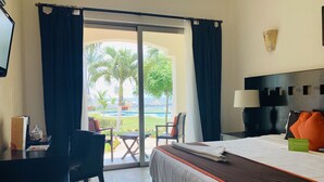 Habitación de hotel con cama, escritorio, silla y vista a una piscina y palmeras.