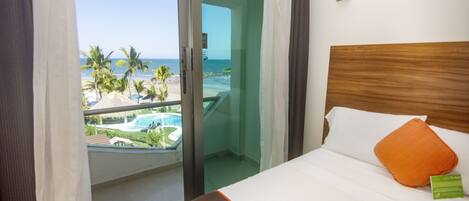 A hotel room with a bed, a view of the beach, and a pool.
