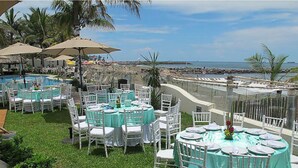 Un espacio de comedor al aire libre con mesas y sillas redondas, con vista a una playa y el océano.