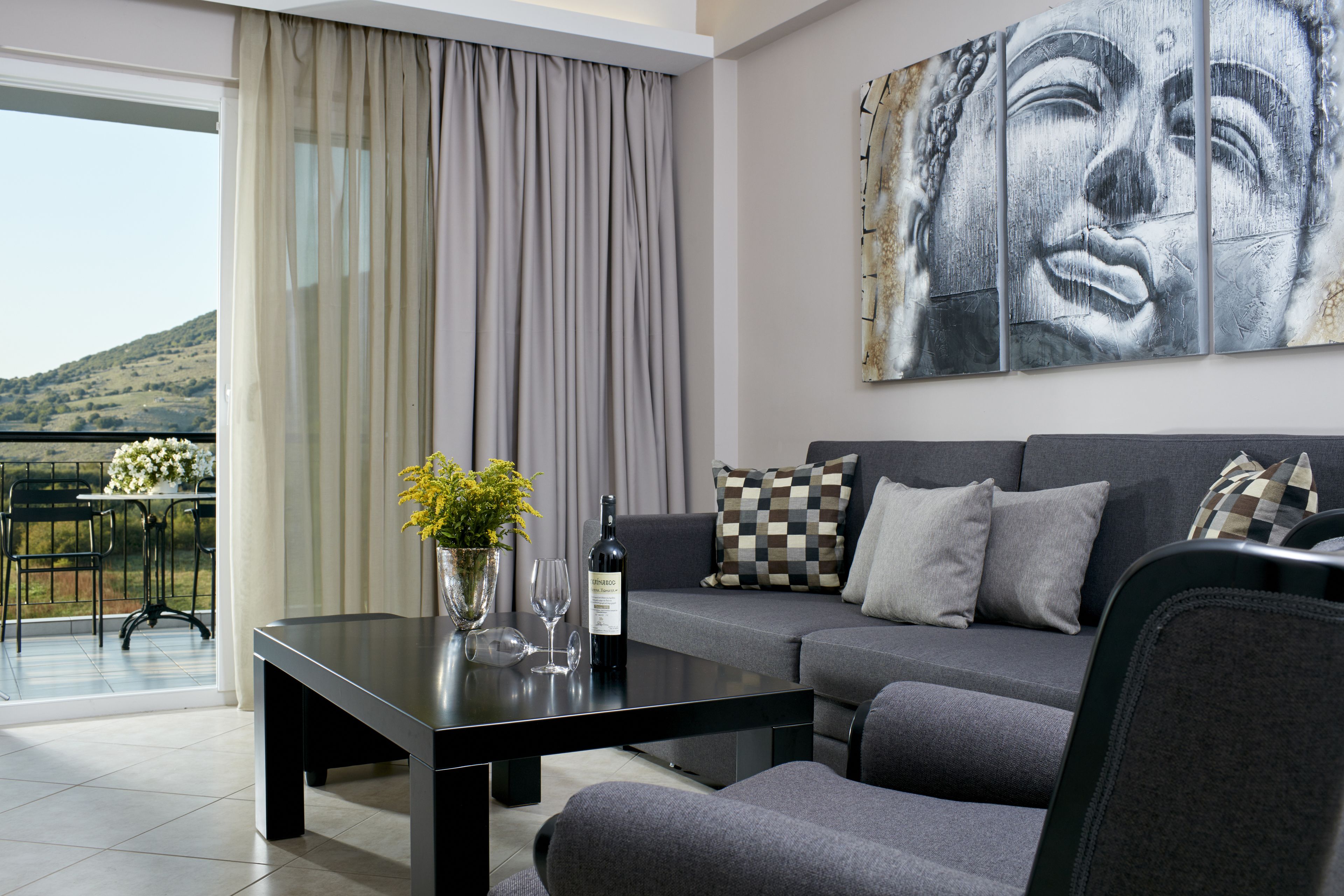 A modern living room with a sofa, a coffee table, and a view of a balcony with a table and chairs.