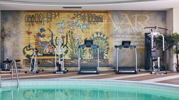 A swimming pool area with exercise equipment and a mural depicting ancient Egyptian art.