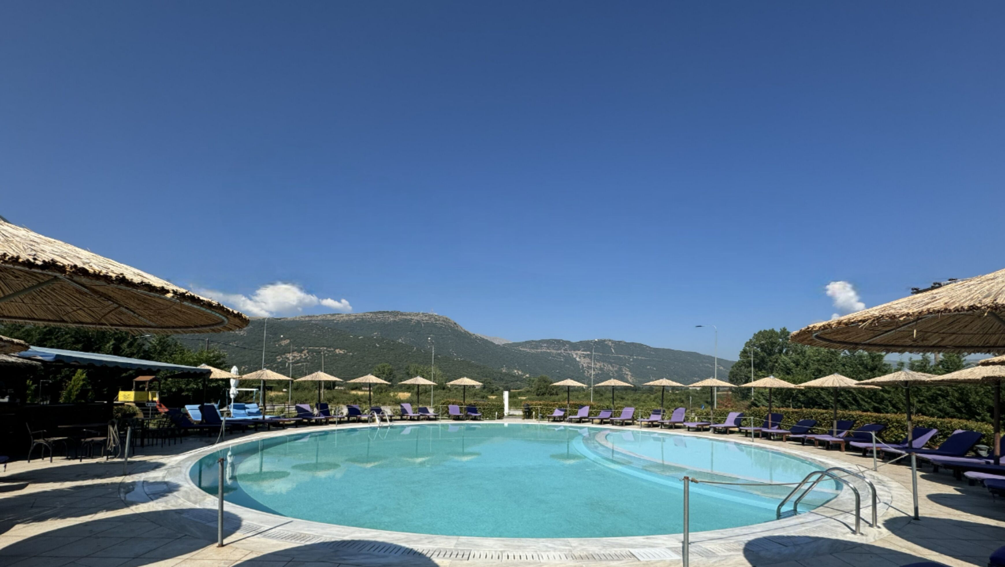 Una piscina con sillones de descanso y sombrillas, rodeada de montañas.