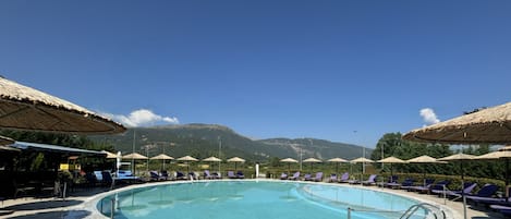 Una piscina con sillones de descanso y sombrillas, rodeada de montañas.