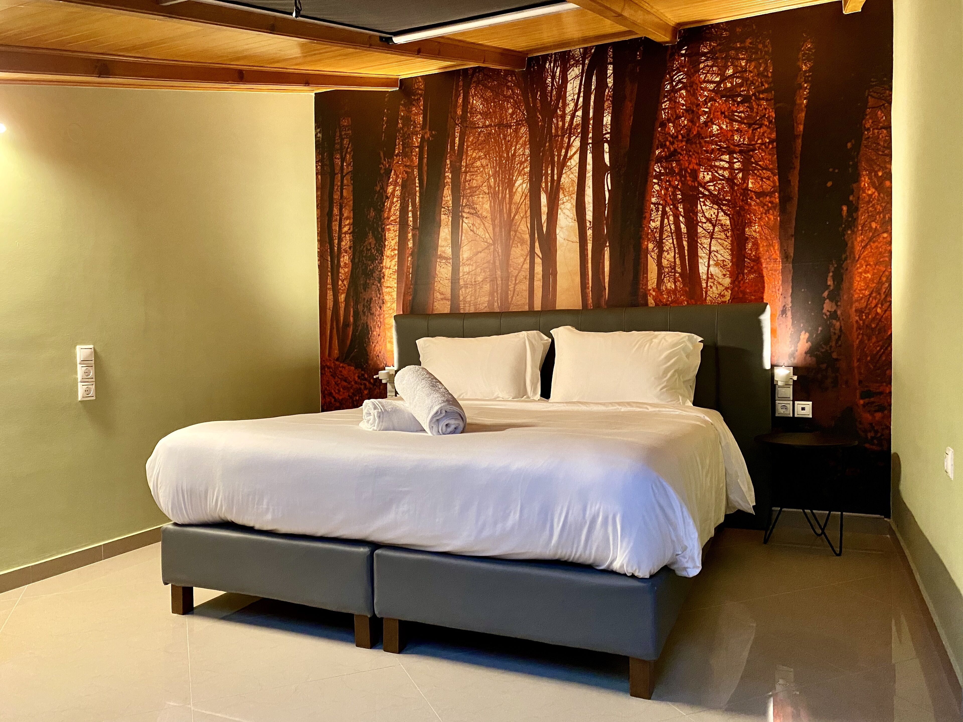 Una habitación de hotel moderna con una cama grande, una mesita de noche y un mural en la pared con un bosque.