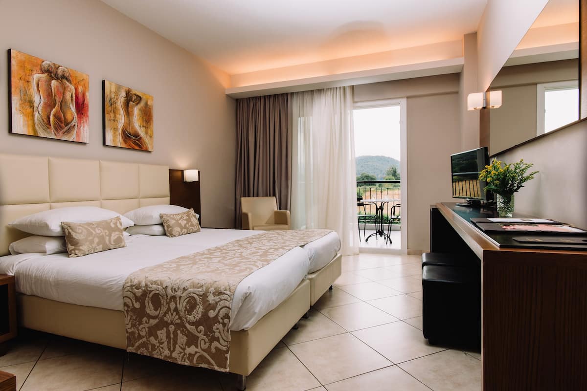 A hotel room with a large bed, a desk, a chair, and artwork on the wall.