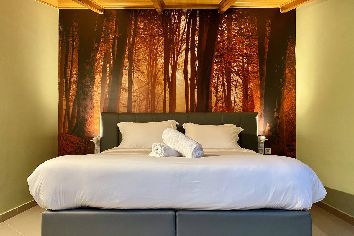 A large bed with a headboard, two bedside tables, and a rolled towel on the bed.